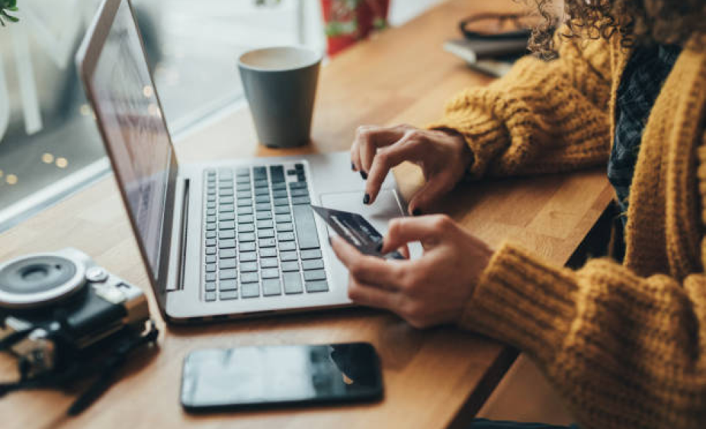 Person entering credit-card details on a laptop at a wooden desk with camera and coffee nearby