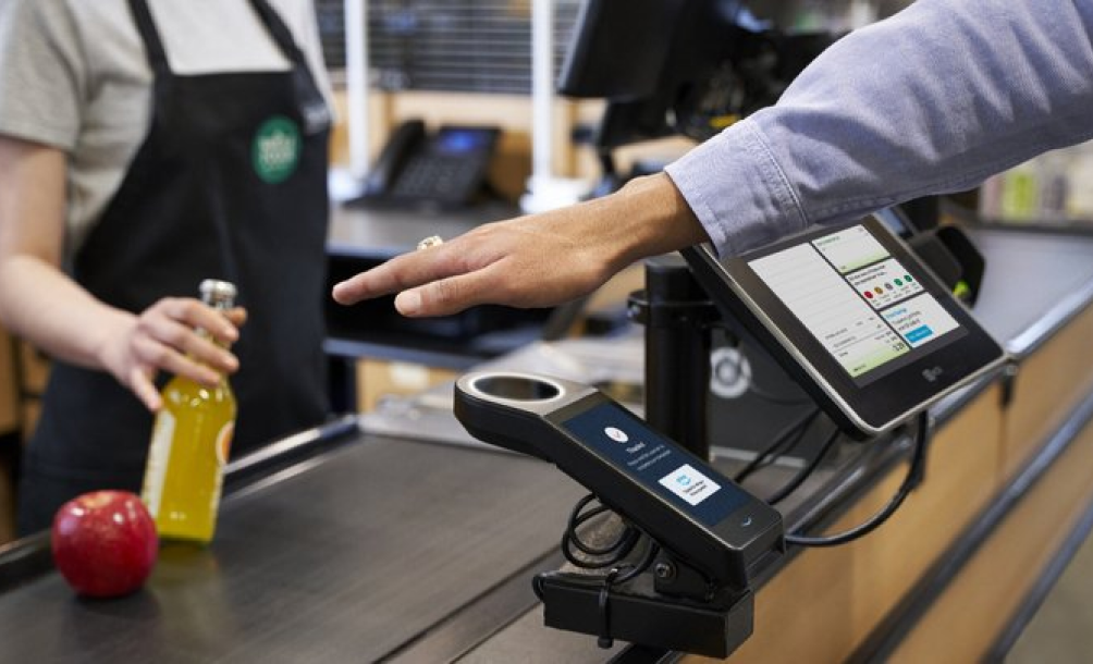 Customer tapping a contactless card reader at a grocery checkout counter