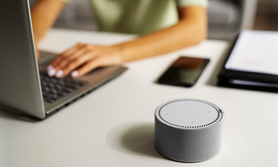 Smart speaker on a desk next to a laptop and smartphone, symbolizing voice-activated shopping in a connected home.