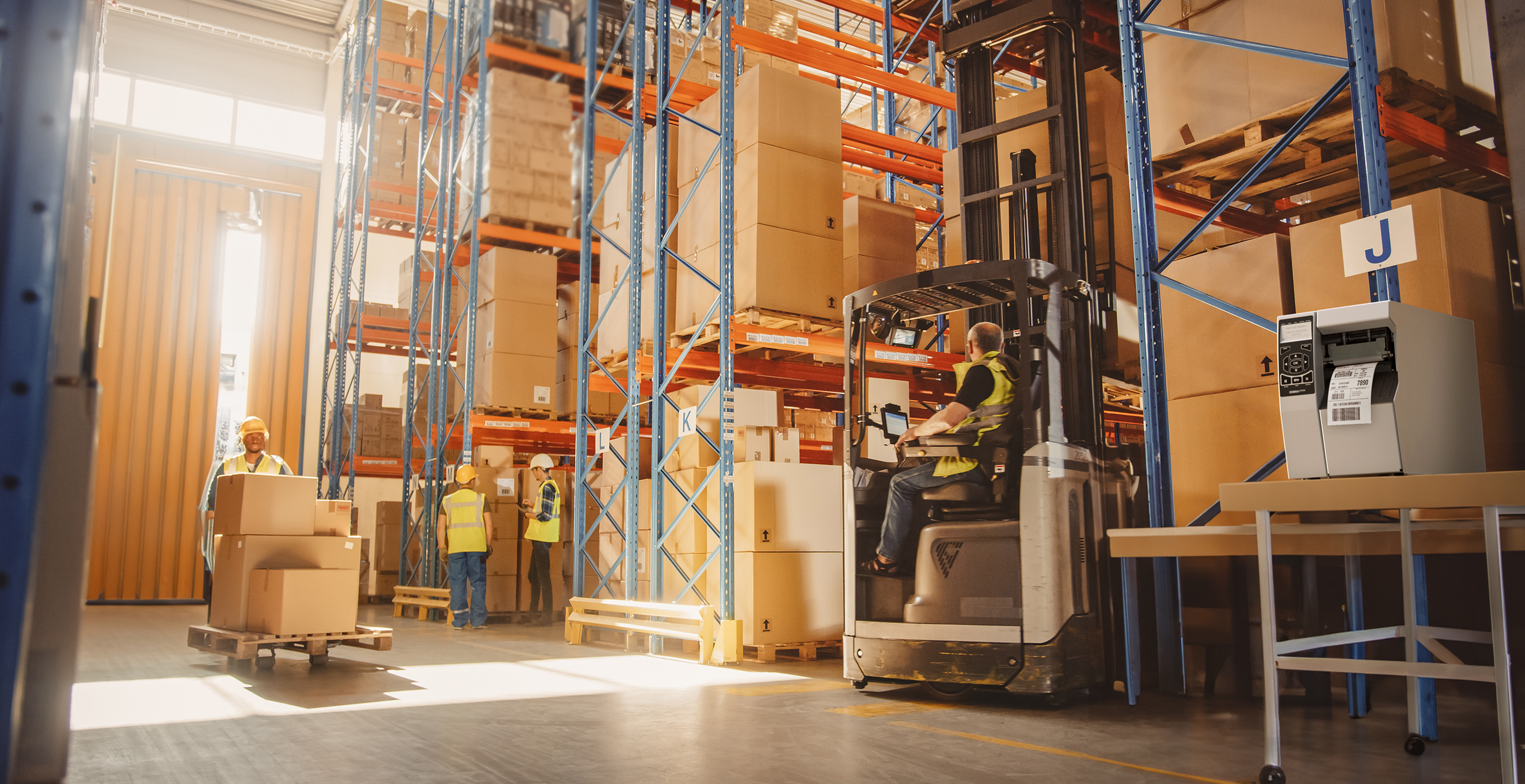 Modern warehouse with forklift operators managing boxed inventory for endpoint device rollout.