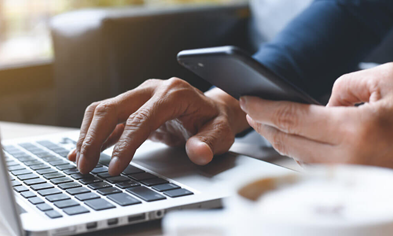Close-up of hands multitasking between laptop and smartphone, representing an omnichannel digital shopping experience.