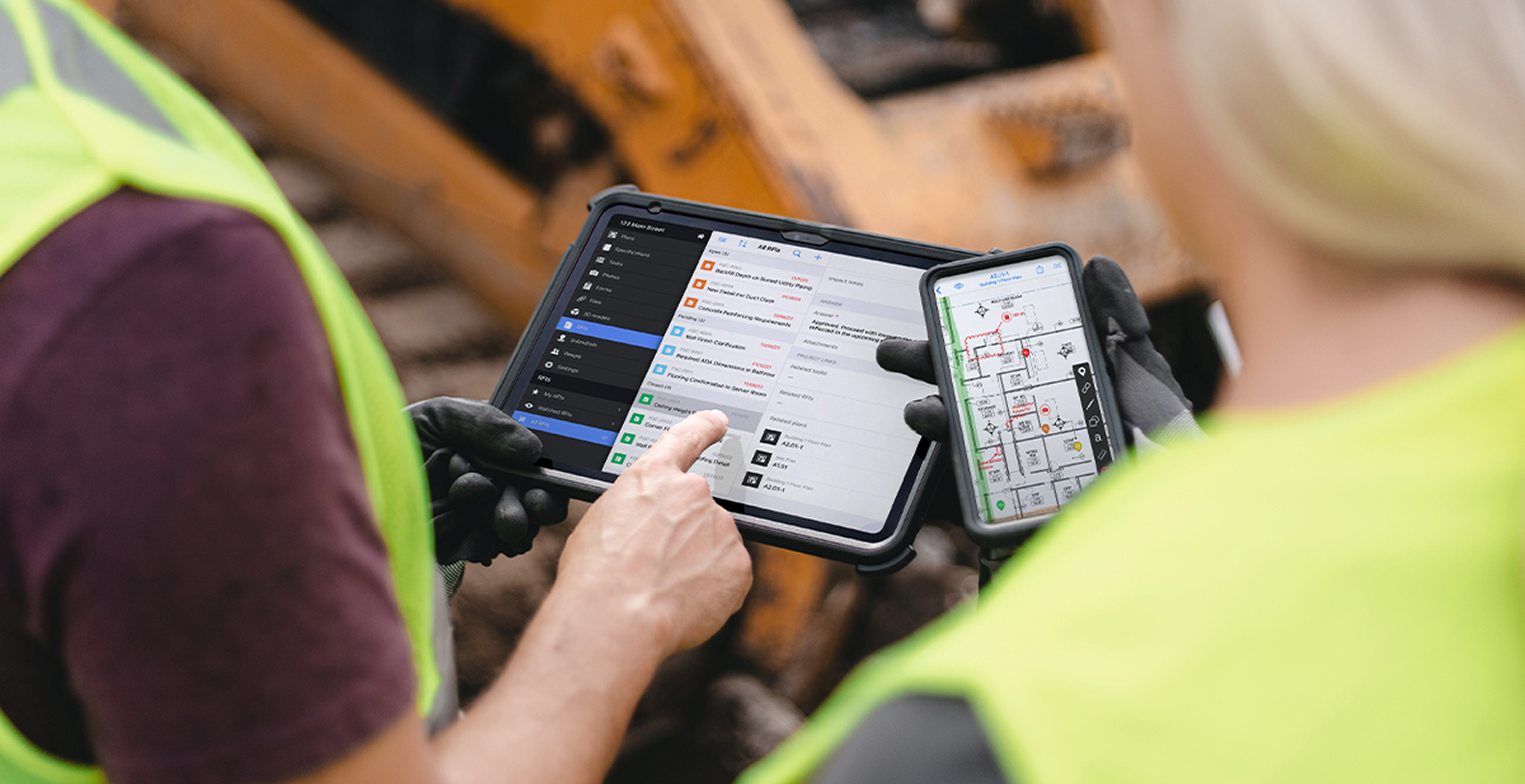 field technicians reviewing site plans on tablet and smartphone in high-visibility vests at construction site