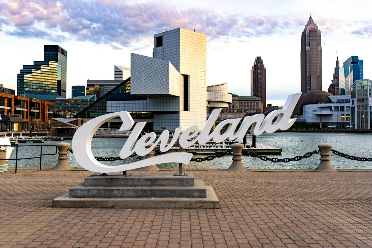 White script Cleveland sign on the lakefront with the Rock and Roll Hall of Fame and downtown Cleveland skyline behind it